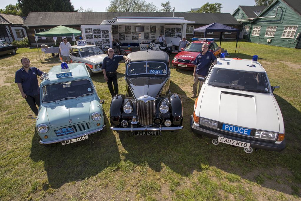 Group of men posing with vintage police cars in a sunny outdoor setting.