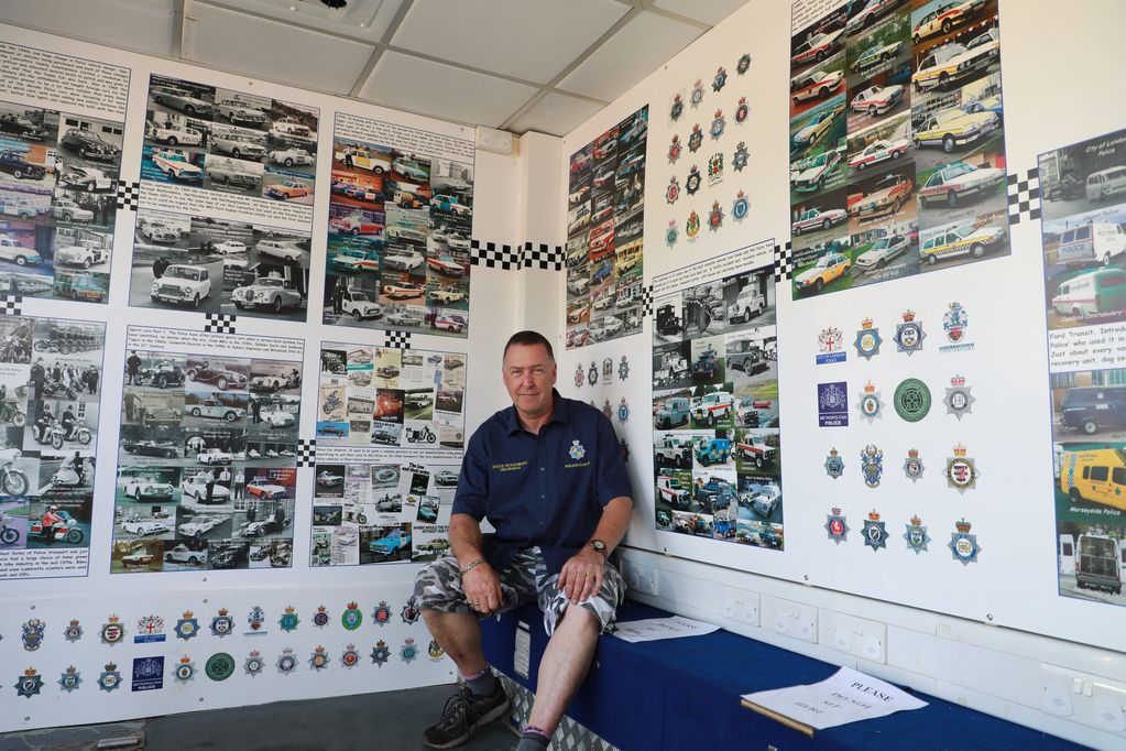 Man sitting in a room filled with vintage police car and badge displays.
