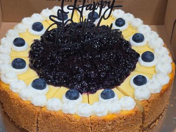 Cheesecake with fresh blueberries and blueberry reduction in a display box.