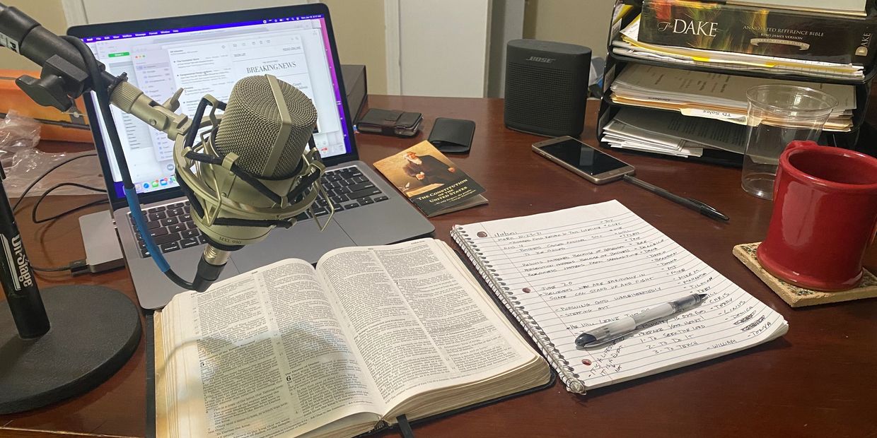 Desk setup with a microphone, open Bible, notebook, and laptop for recording or studying.