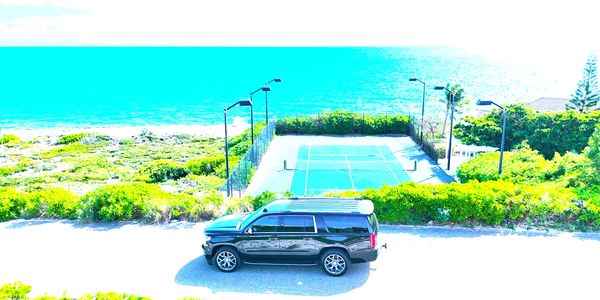 Black SUV parked near tennis courts by the ocean on a sunny day.