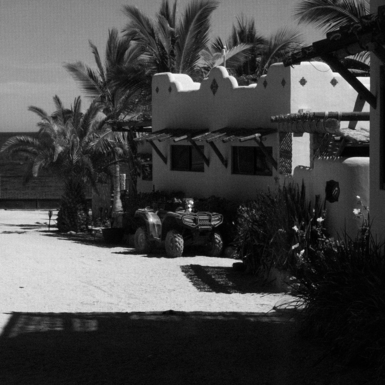 Black and white image of a rustic adobe house with a quad bike parked outside.