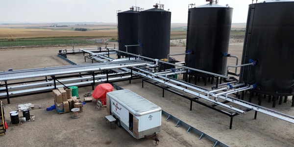 Industrial site with large black storage tanks and interconnected pipelines in a rural area.