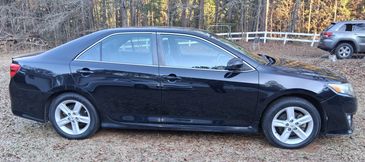 Side view of a black Toyota Camry parked on grass near trees.