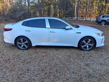Side view of a white Kia sedan parked on grass with trees in the background.