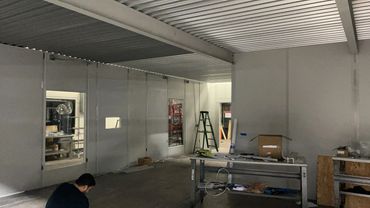 A grey modular office building with beams holding the roof deck and a wall with several windows