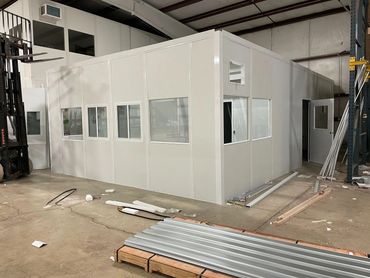 A prefab two story modular office building installation in progress inside a warehouse setting