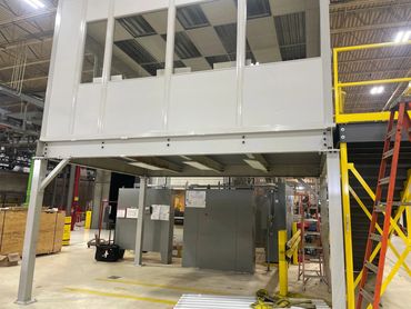 A prefab office being constructed on a mezzanine with windows all around & set of yellow stairs