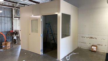 A modular office building with a door and a window installed inside a warehouse or industrial space.