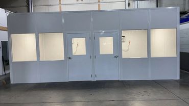 A white, modular, prefabricated room with two doors and four windows inside an industrial warehouse