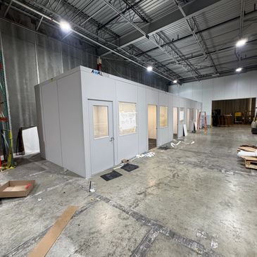 A new row of several prefabricated office solutions and modular offices with windows, doors built inside a warehouse setting.