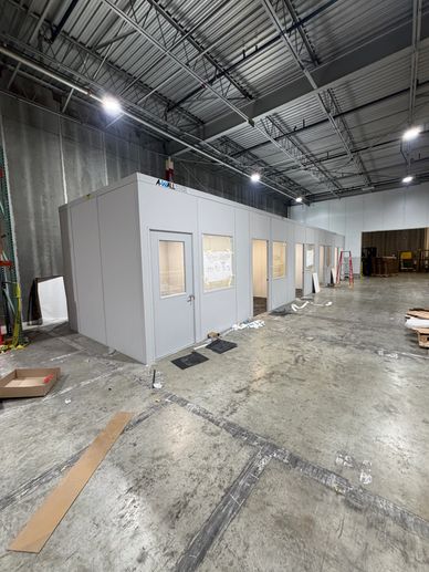 A row of newly built modular office buildings with windows & doors inside a warehouse for employees