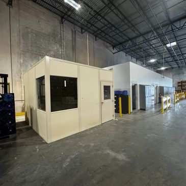 A beige modular office with several windows and a door situated inside a warehouse setting, by SoFlo
