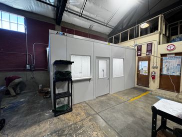 A grey modular office building with several windows and a door, built inside an industrial setting.