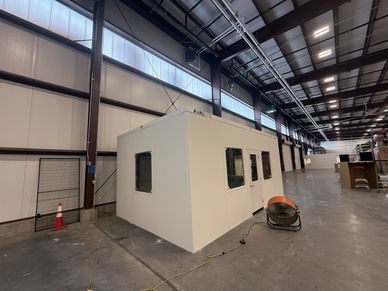 A modular office with windows and a door, installed inside a large industrial warehouse by SoFlo