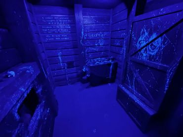 A dark, eerie room with ominous writings and a lifeless figure under blue light.