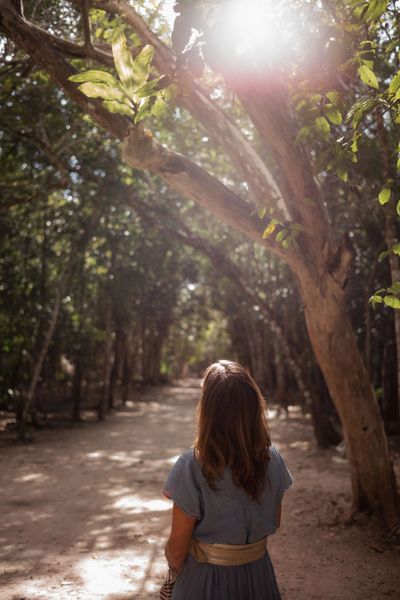 Woman walking through sunlit forest path.