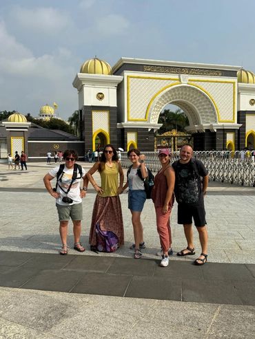 A group of five tourists posing in front of a grand archway with golden domes.