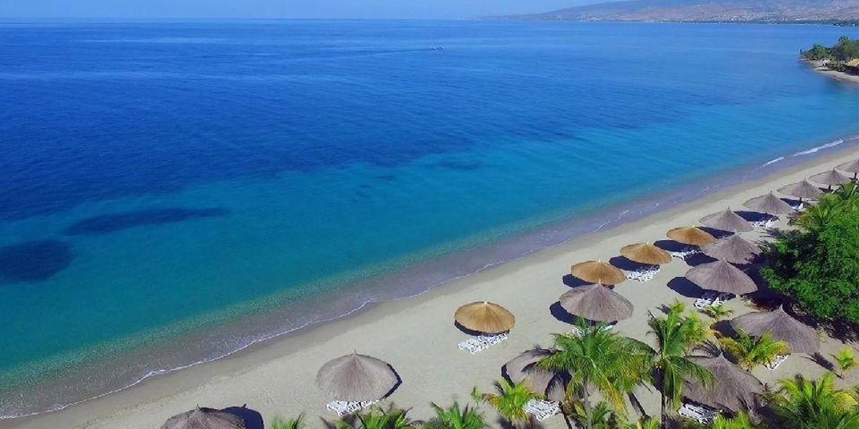 A tranquil beach with clear blue water and straw umbrellas.
