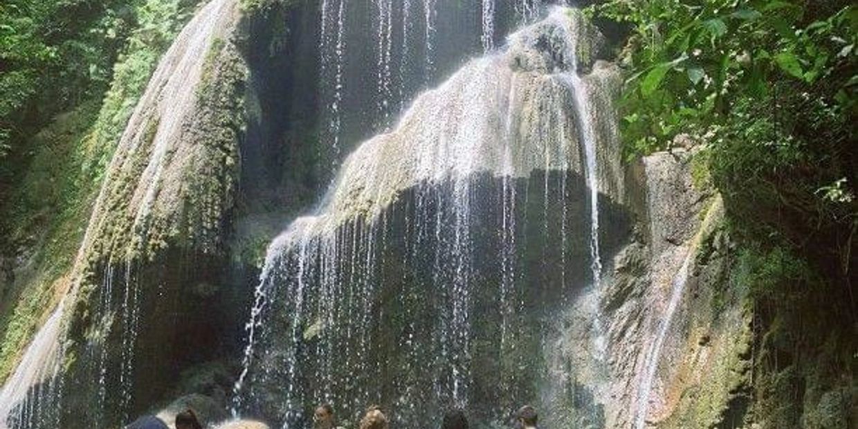 People enjoying a refreshing waterfall in a lush green forest.