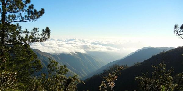 Mountain landscape with clouds floating over valleys under a clear blue sky.