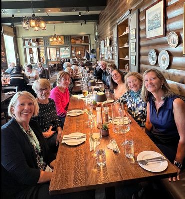 Group of women smiling around a long wooden dining table in a cozy restaurant.