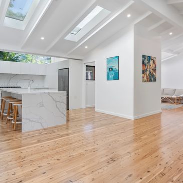A renovation of a kitchen and lounge area. Exposed ceiling rafters all painted white