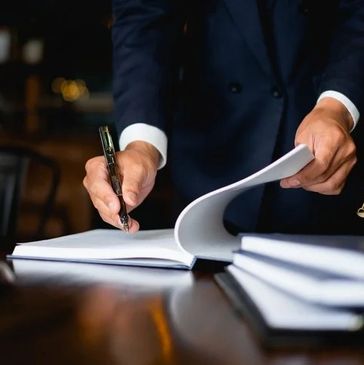 A person in a suit signing legal documents at a desk with law symbols.
