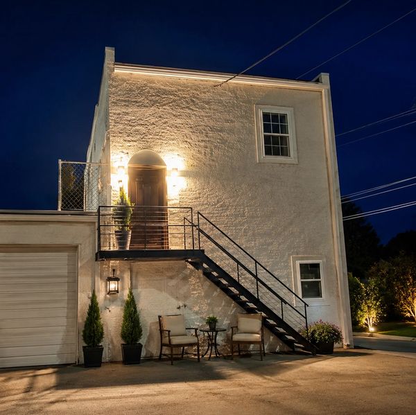 Well-lit modern house exterior at night with stairs and patio furniture.