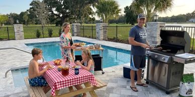 Family enjoying a barbecue by the pool on a sunny day.