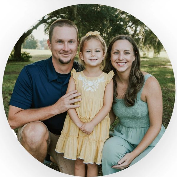 Smiling family of three outdoors on a sunny day.