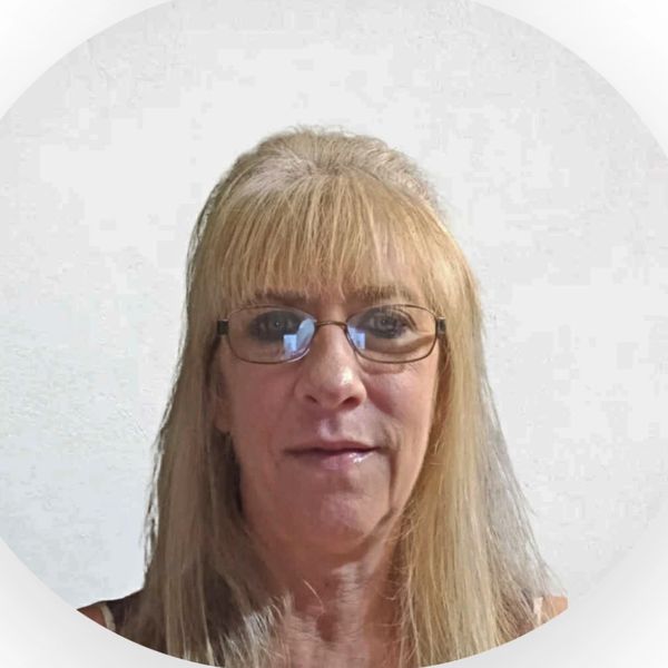 A woman with blonde hair and glasses smiling against a plain background.