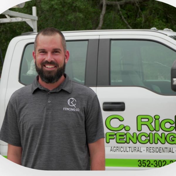 Smiling man in branded polo stands by company truck with fencing logo.
