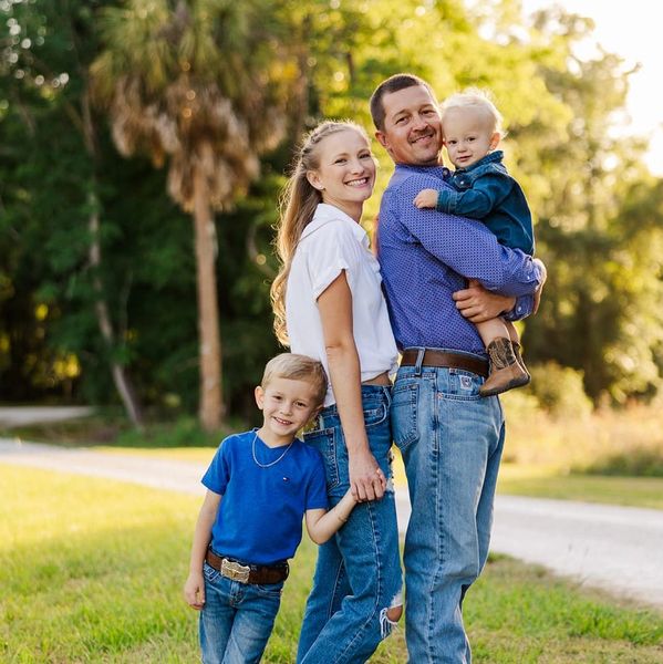 A happy family of four posing outdoors on a sunny day.
