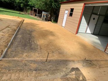 A construction site with a newly prepared dirt foundation next to a metal building.