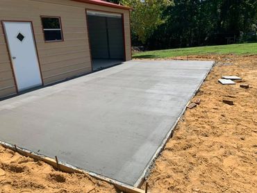 Freshly poured concrete slab beside a building under construction.