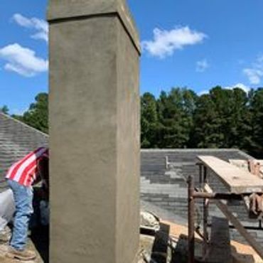 Construction worker plastering a column outside a house under a clear sky.