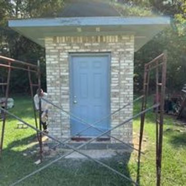 Small brick structure with a blue door under construction in a yard.