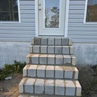 Concrete block stairs leading to a white door on a house exterior.