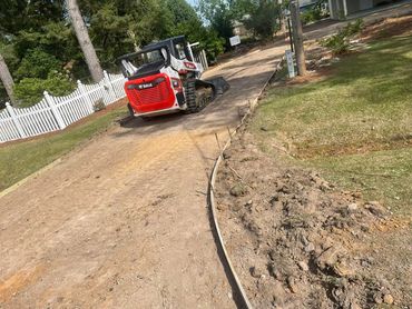 A Bobcat machine preparing a driveway with soil and wooden framing.