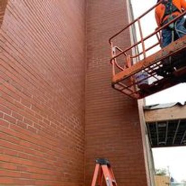 Worker on lift inspecting or repairing a tall brick wall outdoors.