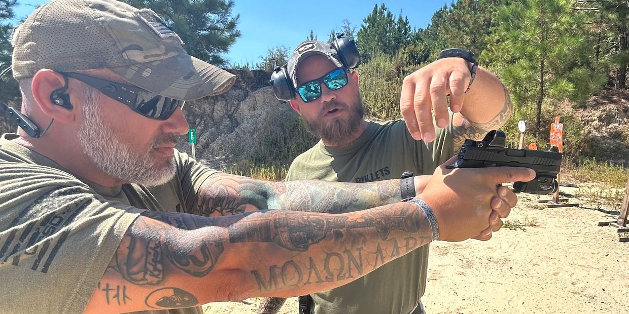 Two men at a shooting range, one instructing the other.