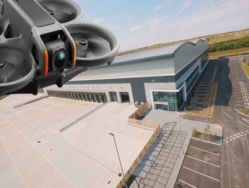 A drone flying near a large warehouse building under a clear sky.