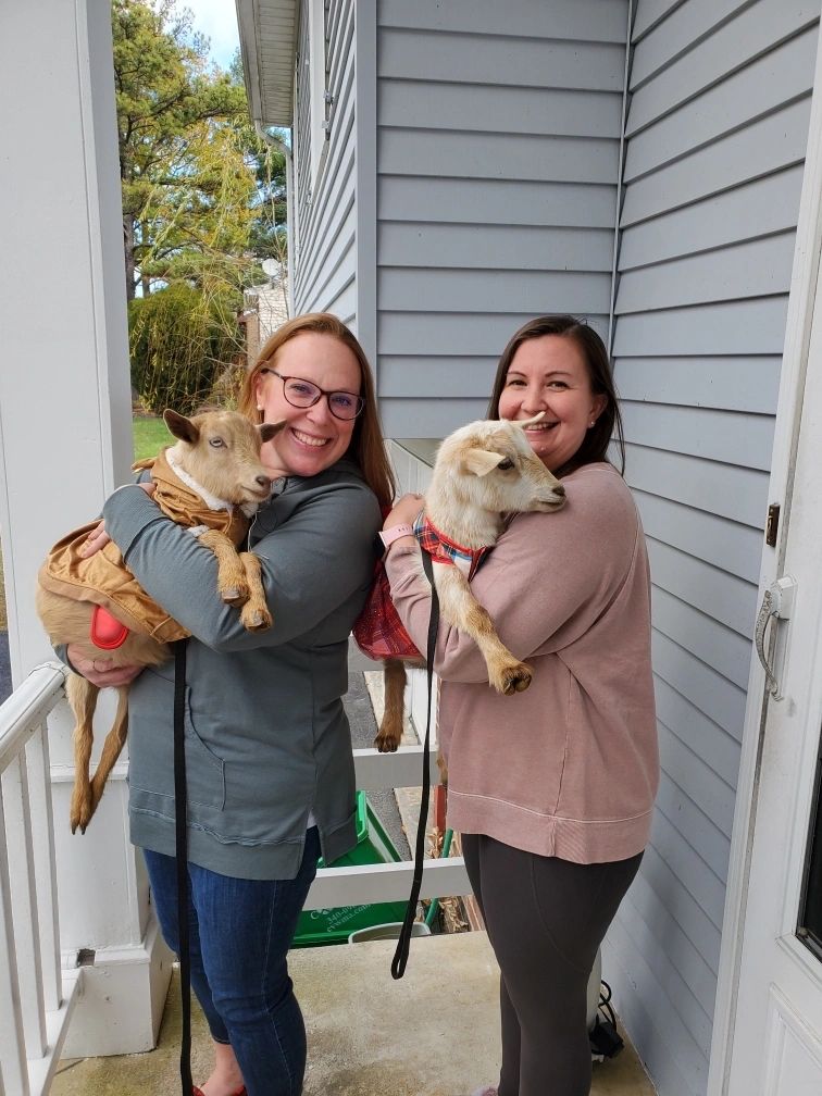 Two women smiling and holding goats dressed in coats.