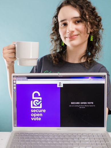bianca with a cup of coffee behind her laptop with the Secure Open Vote website