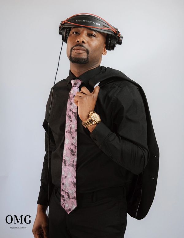 Confident man in black attire with headphones and pink tie.