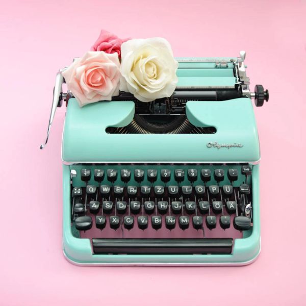 Vintage turquoise typewriter with roses on a pink background.