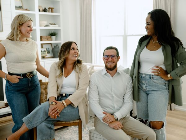 Group of four colleagues smiling and interacting in a modern living room.