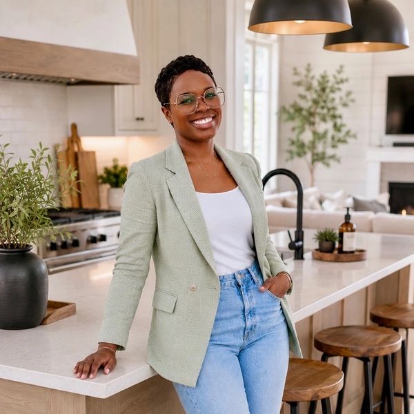 Smiling woman in glasses leaning on a kitchen counter in a stylish modern kitchen.