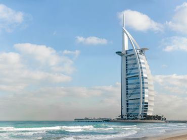 Luxury Burj Al Arab hotel stands on the shore in Dubai, United Arab Emirates with clear blue skies.